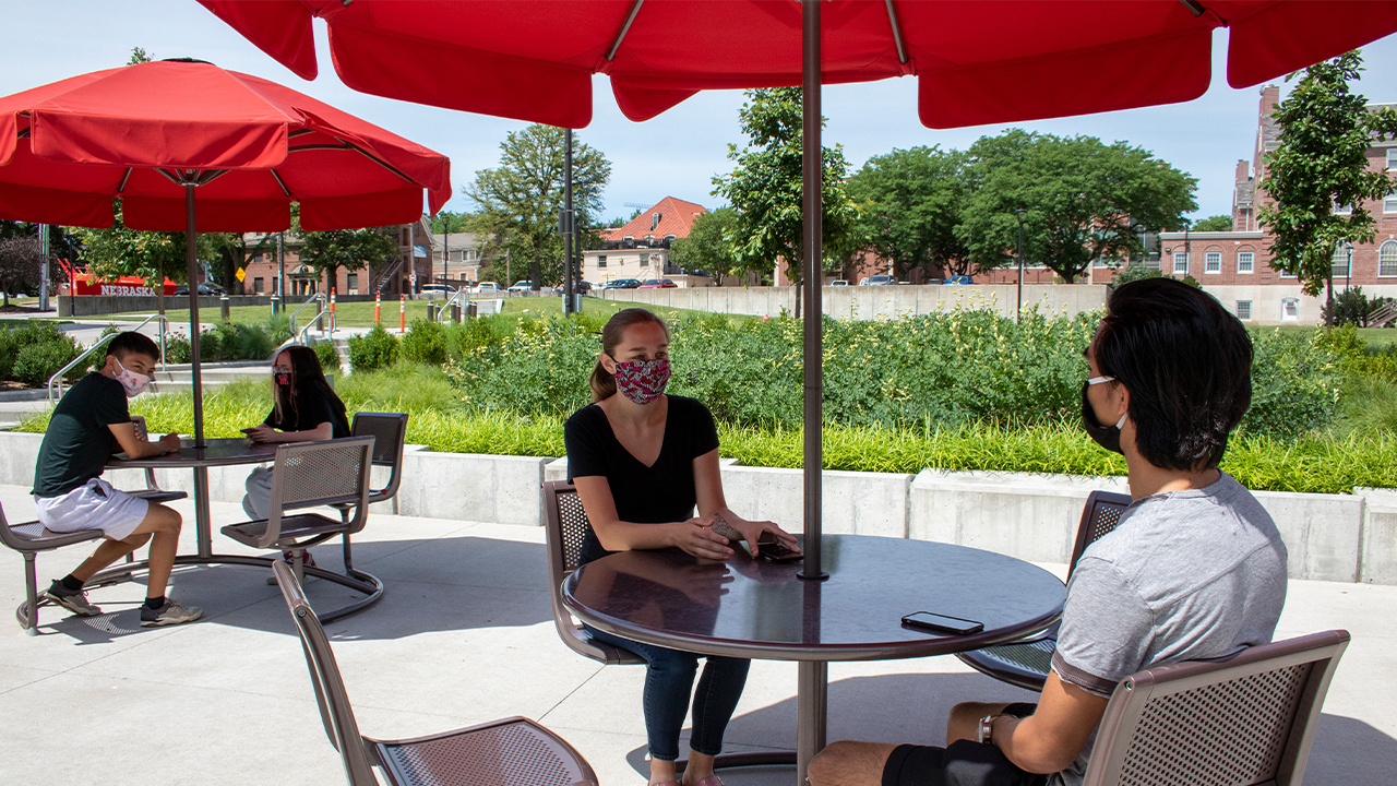 Students wearing COVID-19 masks sitting at a table under an umbrella