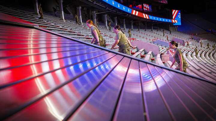 Soldiers ascend stadium stairs under vibrant red, white, and blue lights.