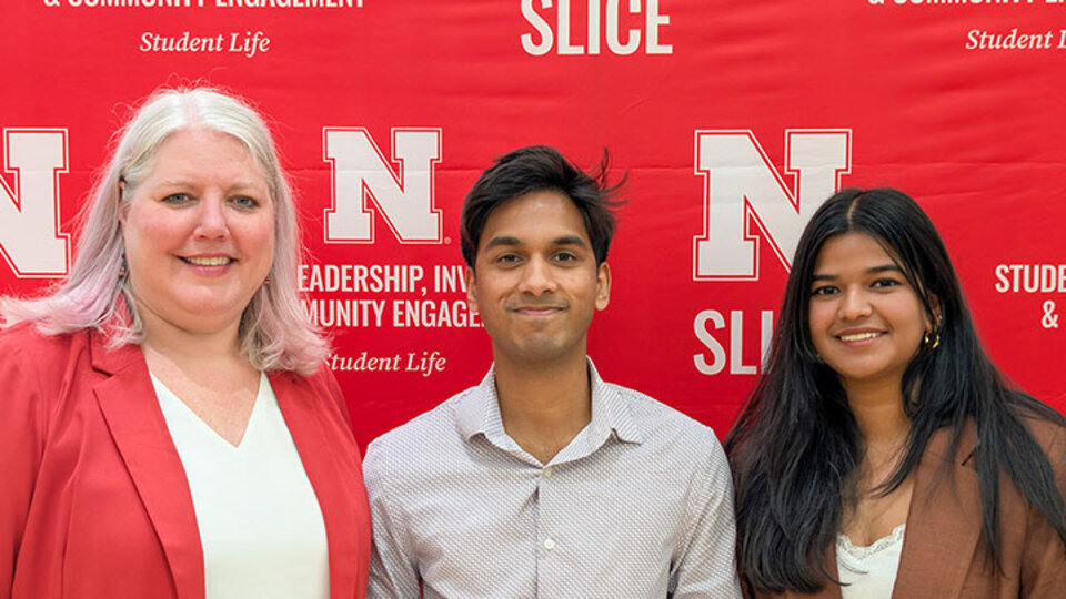 Three people smiling against a red backdrop with university-themed text.