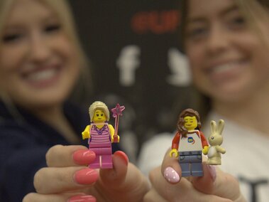 Two women holding LEGO figurines; one is a princess with a wand, the other with a bunny.